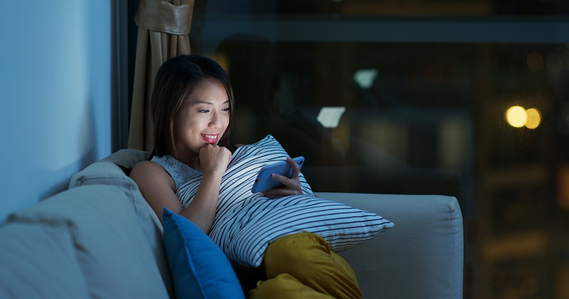 Chica mirando el móvil en el sofá de noche.